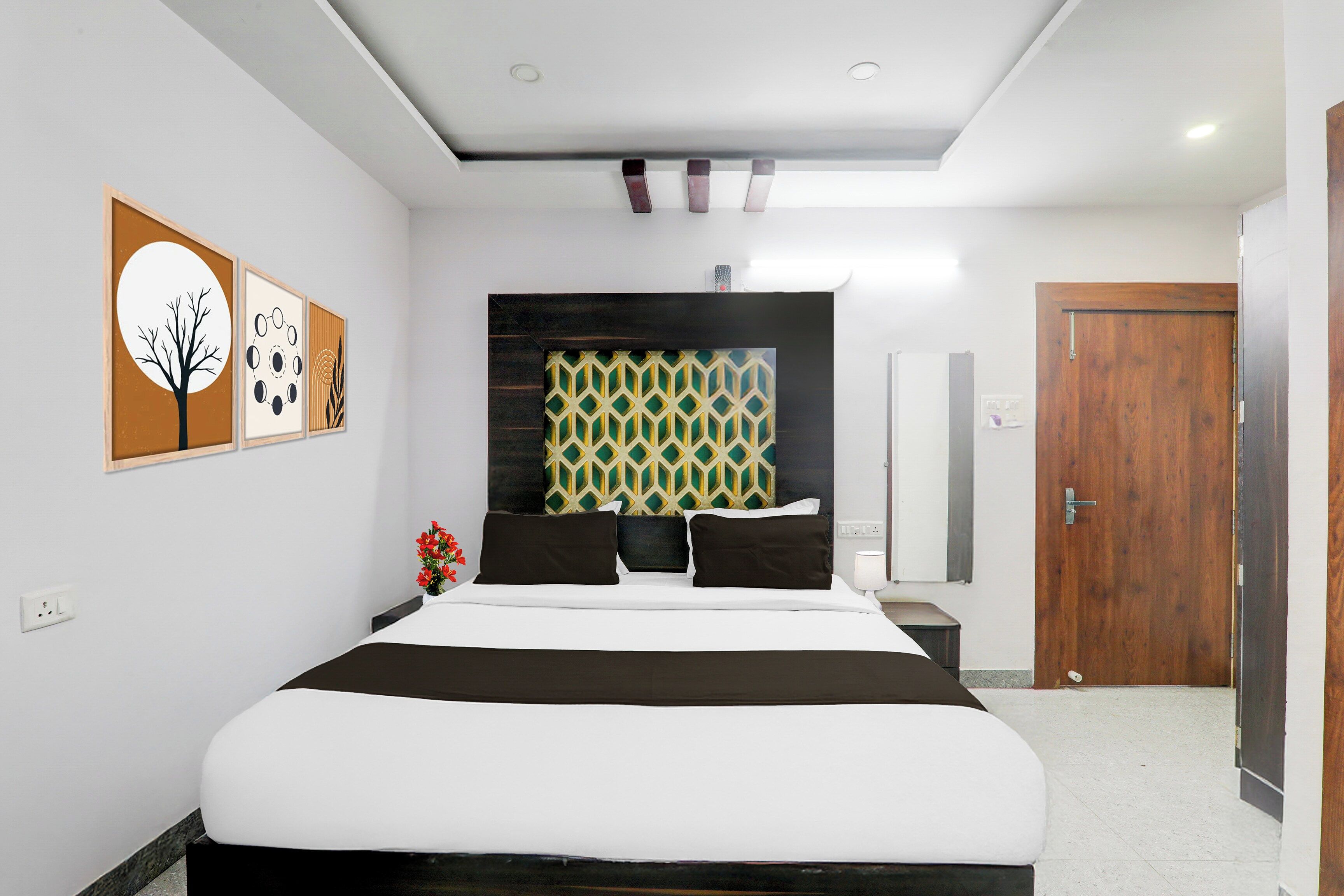 A modern hotel room with a large bed, a headboard with a geometric pattern, and artwork on the walls.
