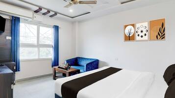 Habitación de hotel con cama, sofá azul, una mesita con bandeja, ventilador de techo y cuadros en la pared.