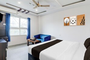 Een hotelkamer met een bed, een blauwe bank, een klein tafeltje met een dienblad, een plafondventilator en kunst aan de muur.