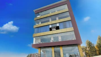 Un edificio de varios pisos con fachada de vidrio, un letrero que indica que es una colección de apartamentos con servicios, y una escalera que conduce a la entrada.
