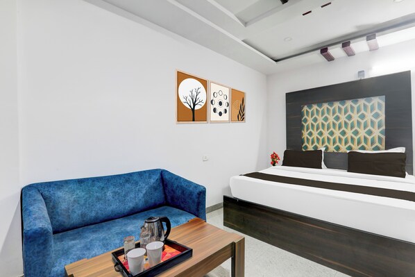 A modern hotel room with a blue sofa, a wooden coffee table with a tray of cups and a kettle, a bed with a patterned headboard, and two wall art pieces. - Collection O Bihar Sharif (Bihar Sharif)