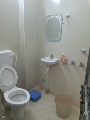 A small bathroom with a toilet, sink, mirror, and a trash bin. - SRG Hotel and Restruant (Dhauru Pur, Mirzapur)