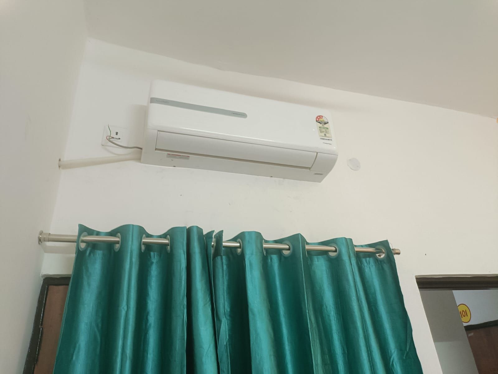 A room with a white air conditioning unit mounted on the wall and a teal curtain rod with a teal curtain.