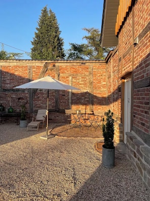Un patio con mesa y sillas, un pequeño jardín y un muro de ladrillo.