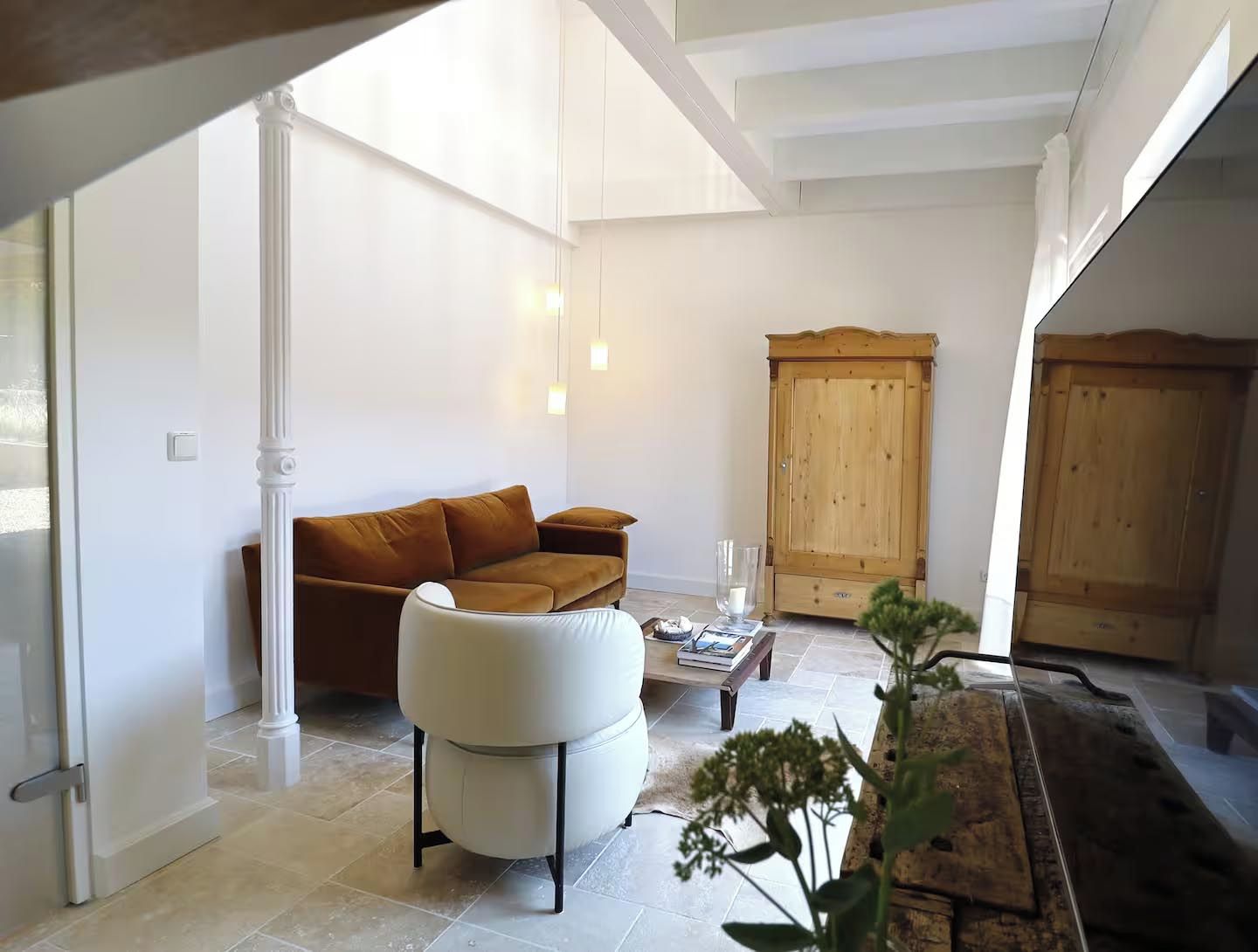 Un salon comprenant un canapé, un fauteuil blanc, un meuble en bois et une table basse avec des livres.
