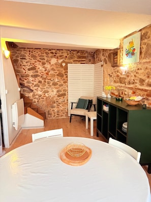 A cozy room with a stone wall, a white table with a decorative centerpiece, a chair, and a small shelf with items. - St Cyprien Cocon in the heart of the village (Saint-Cyprien)