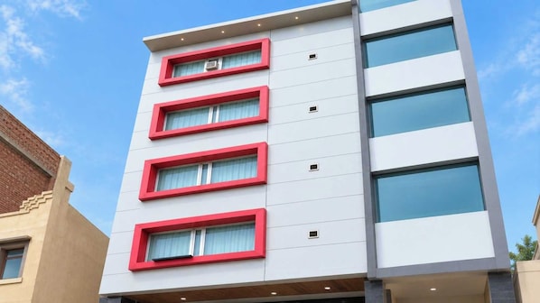 A multi-story building with a modern architectural style, featuring a series of windows with red frames and a flat facade.