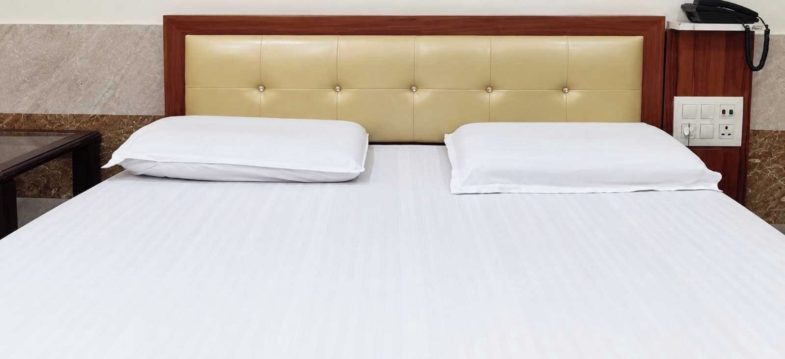 A hotel room with a bed, a bedside table, a telephone, and a wall socket.
