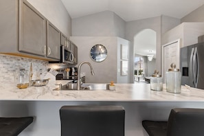 A modern kitchen with a central island, stainless steel appliances, and a large round mirror. - Four Palms Pool Retreat | 4BR, Private Pool & Game (Kissimmee)