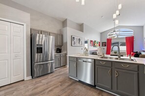 A modern kitchen with stainless steel appliances, grey cabinetry, and a central island with a sink. - Four Palms Pool Retreat | 4BR, Private Pool & Game (Kissimmee)