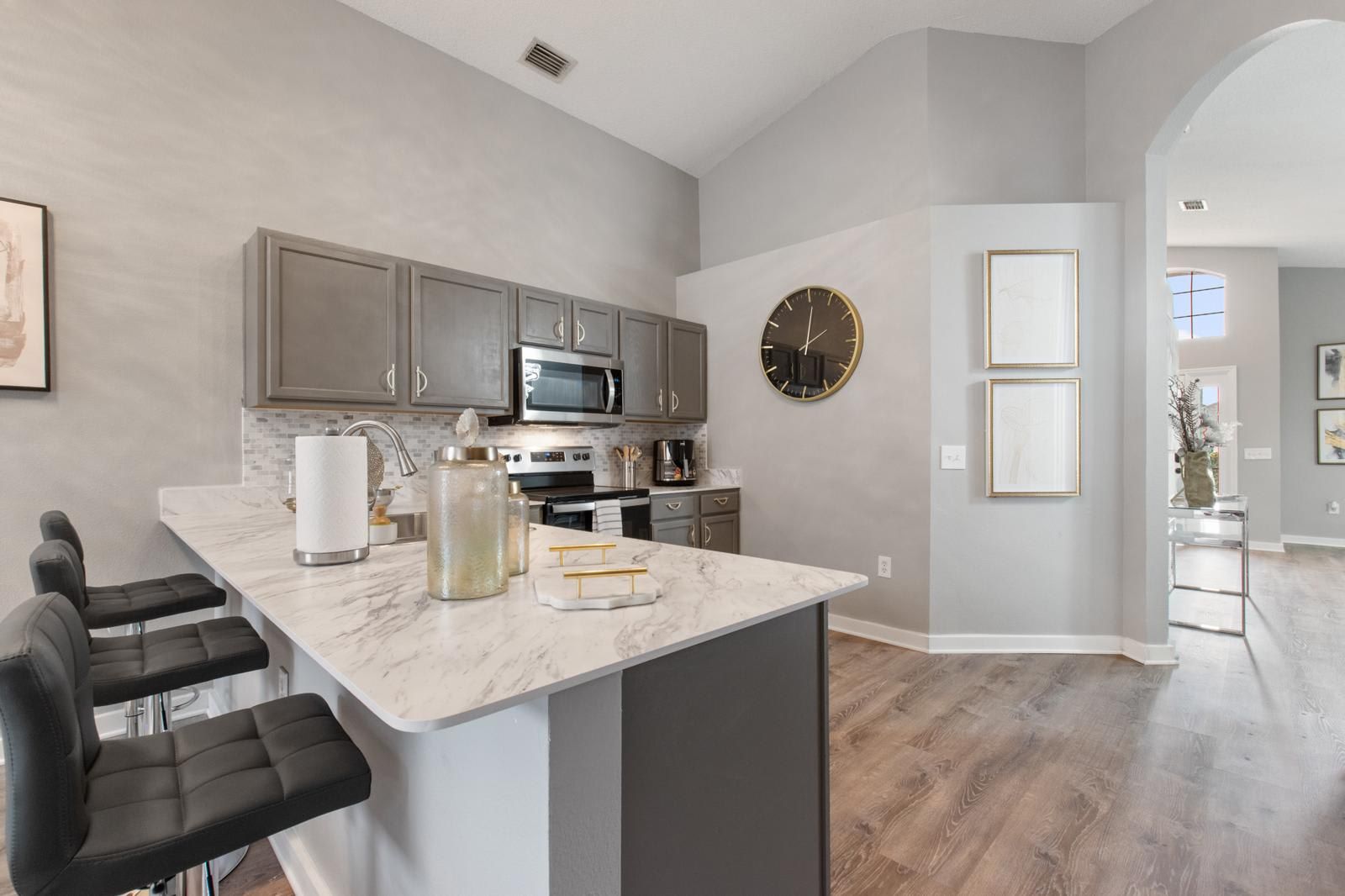 A modern kitchen with a marble countertop, stainless steel appliances, and a large wall clock.