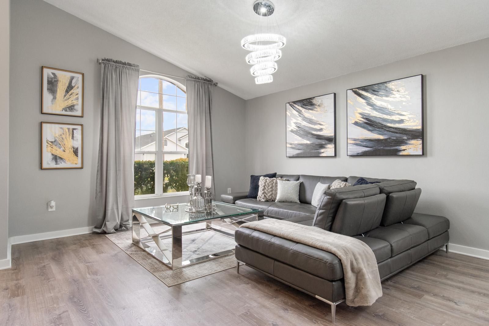 A modern living room with a glass coffee table, grey sofa, and abstract art on the walls.
