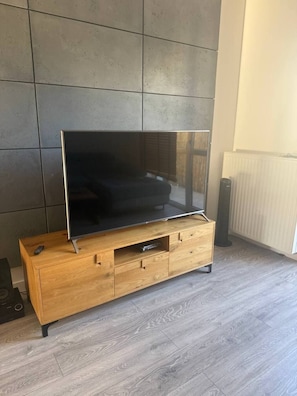 Un suport de televisió de fusta amb un televisor de pantalla plana, un comandament a distància i un altaveu a terra.