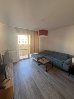 A modern living room with a sectional sofa, a coffee table, and a TV on a wooden stand. - Lumina 2BR Apt w/ Parking & Balcony  (Warszawa)