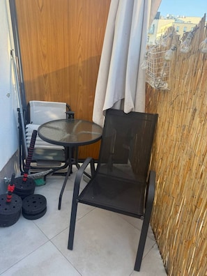 Ein kleiner Sitzbereich im Freien mit einem runden Tisch und zwei Stühlen, einem Besen und einem Paar Hanteln.