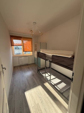 A compact room with a bunk bed, a radiator, a window with blinds, and a ceiling light fixture. - Lumina 2BR Apt w/ Parking & Balcony  (Warszawa)
