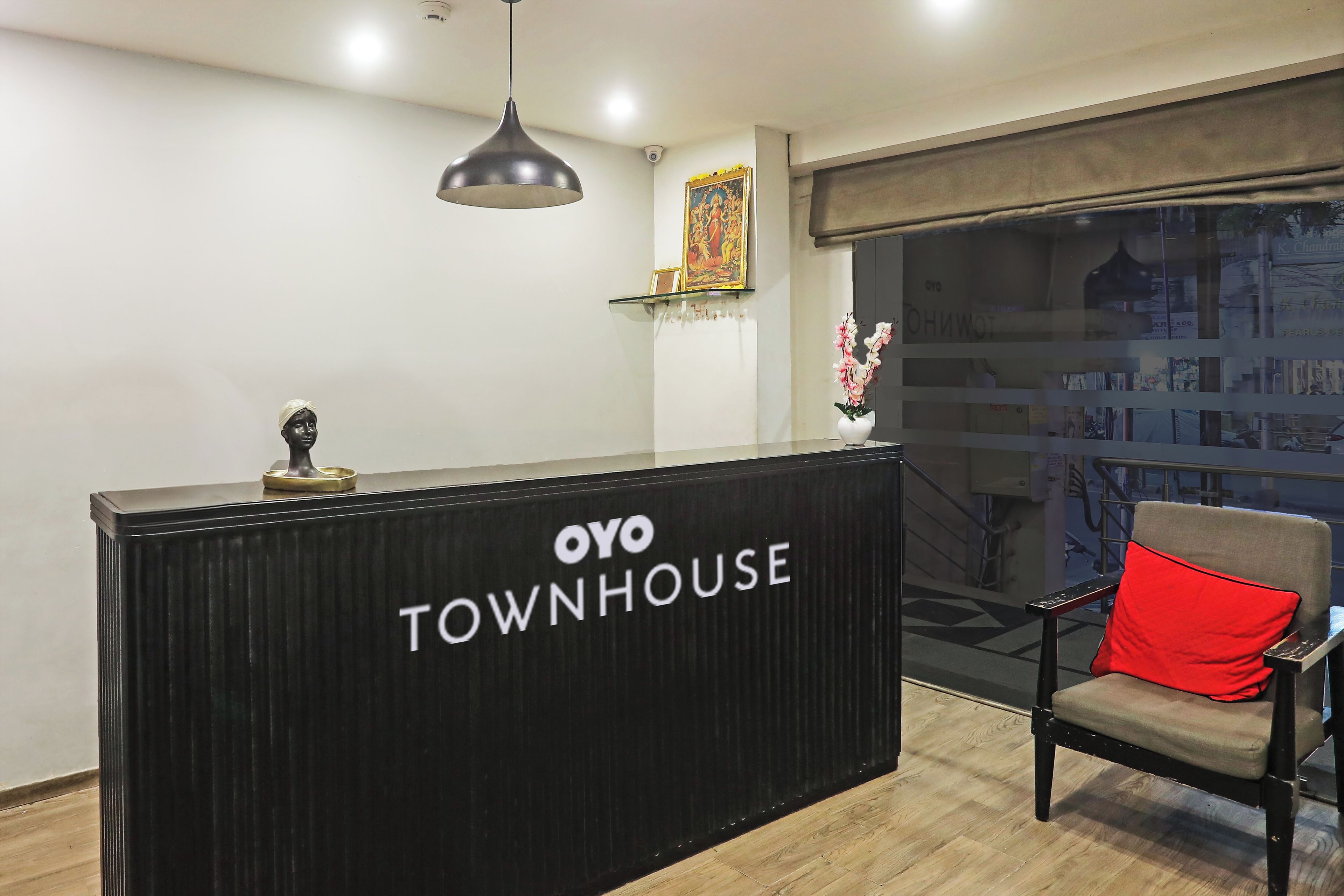 A reception desk with 'OYO TOWNHOUSE' signage, a chair with a red cushion, a pendant light, and a framed picture on the wall.