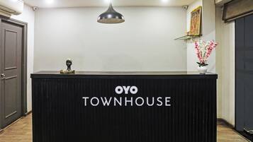 Una recepción con letrero 'OYO TOWNHOUSE', una lámpara colgante, un cuadro en la pared y un florero con flores.