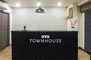 Una recepción con letrero 'OYO TOWNHOUSE', una lámpara colgante, un cuadro en la pared y un florero con flores.