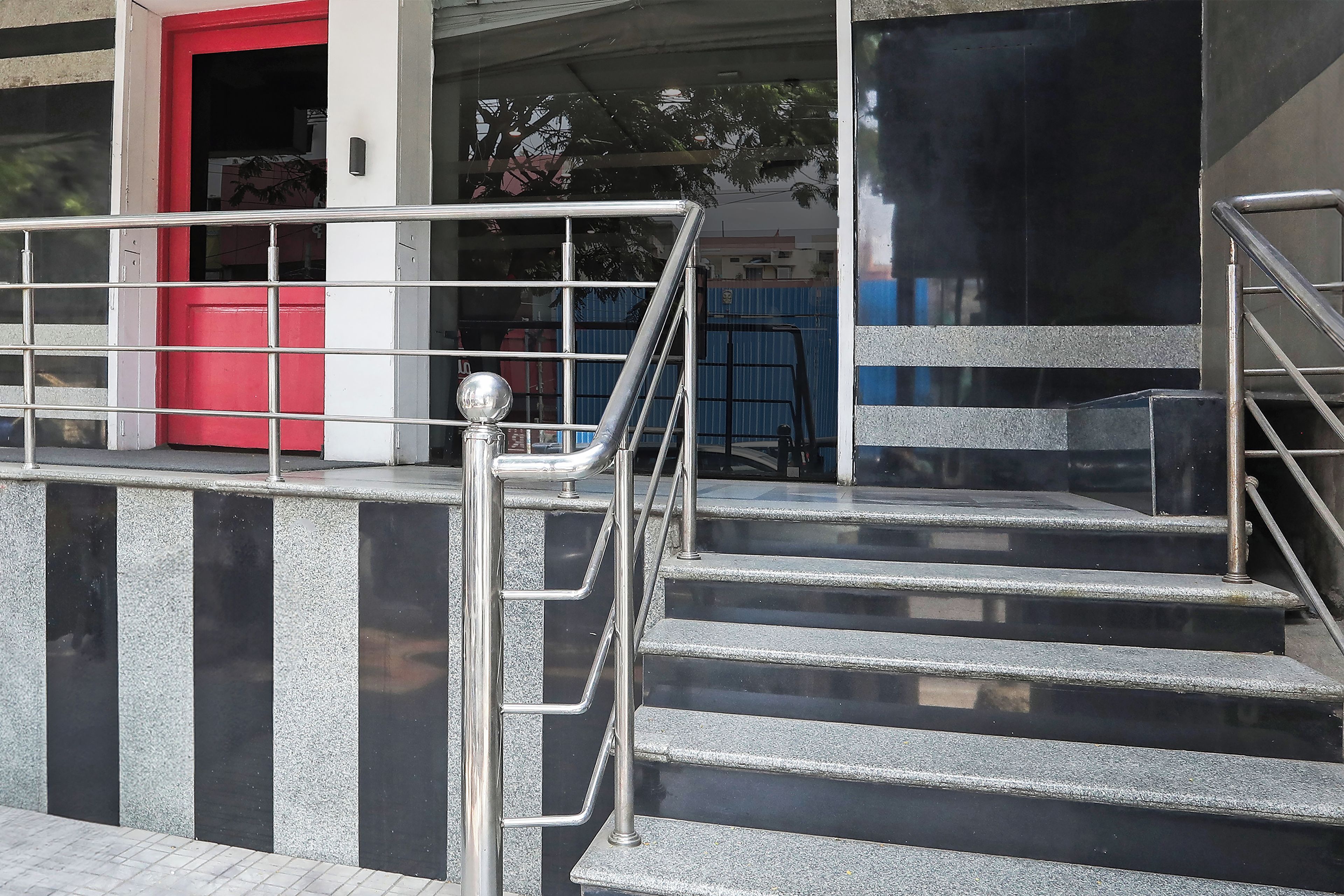 Una escalera conduce a la entrada de un edificio con una puerta roja y barandillas de metal.