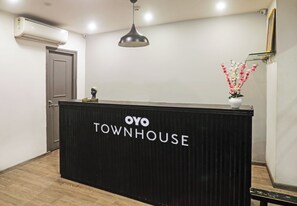Una recepción con letrero 'OYO TOWNHOUSE', un aire acondicionado instalado en el techo, una lámpara colgante y un jarrón con flores.