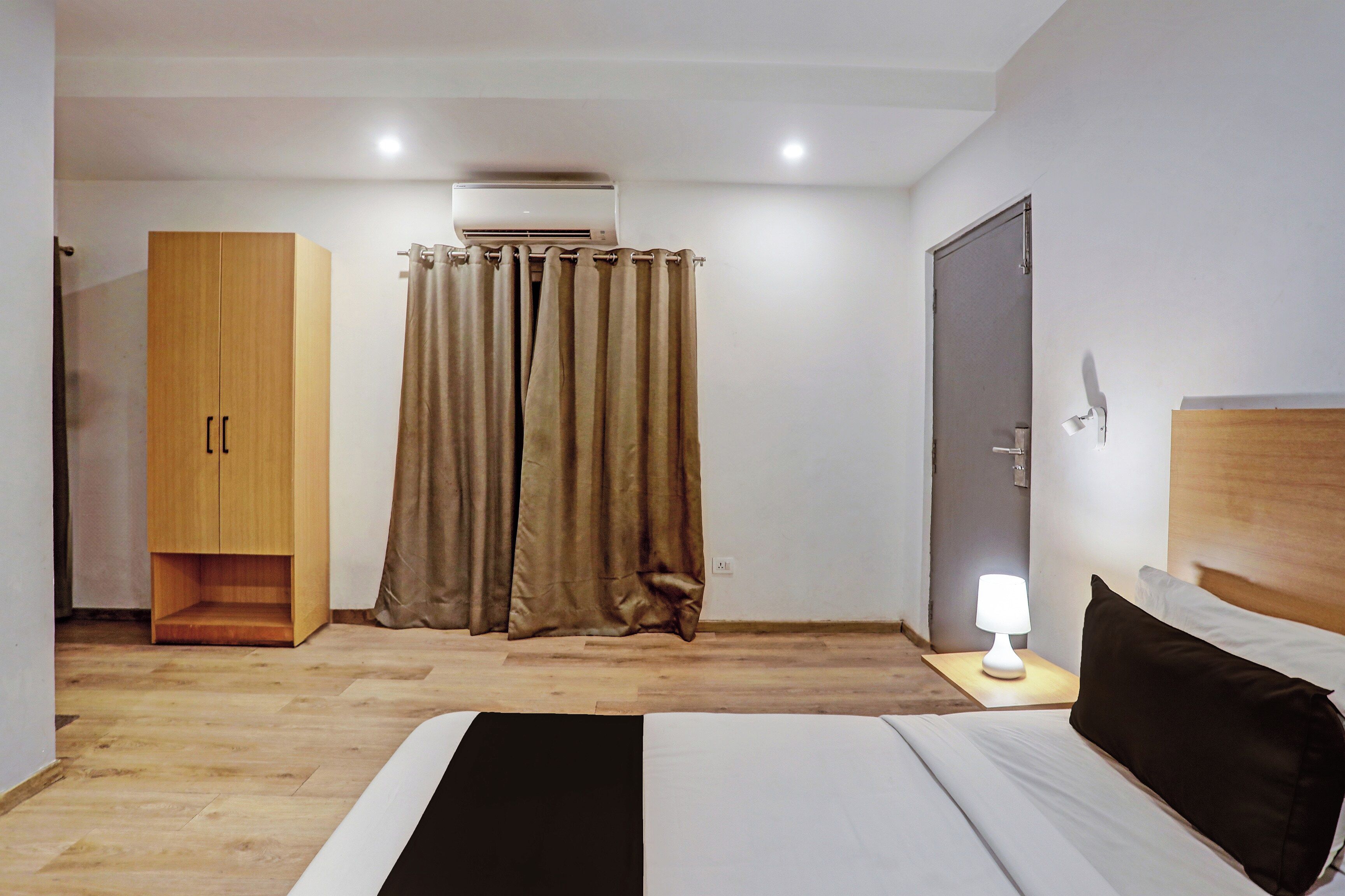A bedroom with a bed, a wardrobe, a curtain, a bedside lamp, and a door.