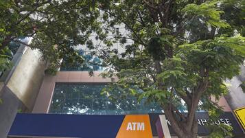 Señal de cajero automático en la fachada de un edificio, con un árbol al frente.