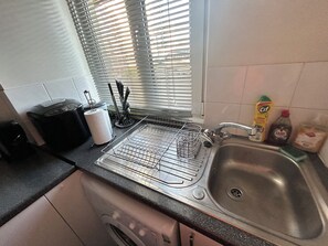 A kitchen with a dishwasher, a sink, and a window with blinds. - Central London Studio Apartment- walking distance from the London Eye/Big Ben (London)