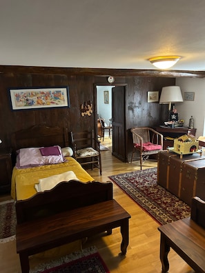 Een kamer met een bed, een houten bankje, een bureau met lamp en een klein scheepsmodel op een tafel.