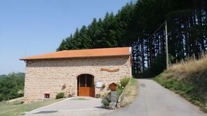 Un bâtiment en pierre avec un toit en tuiles, une porte en bois et un petit porche agrémenté de plantes.