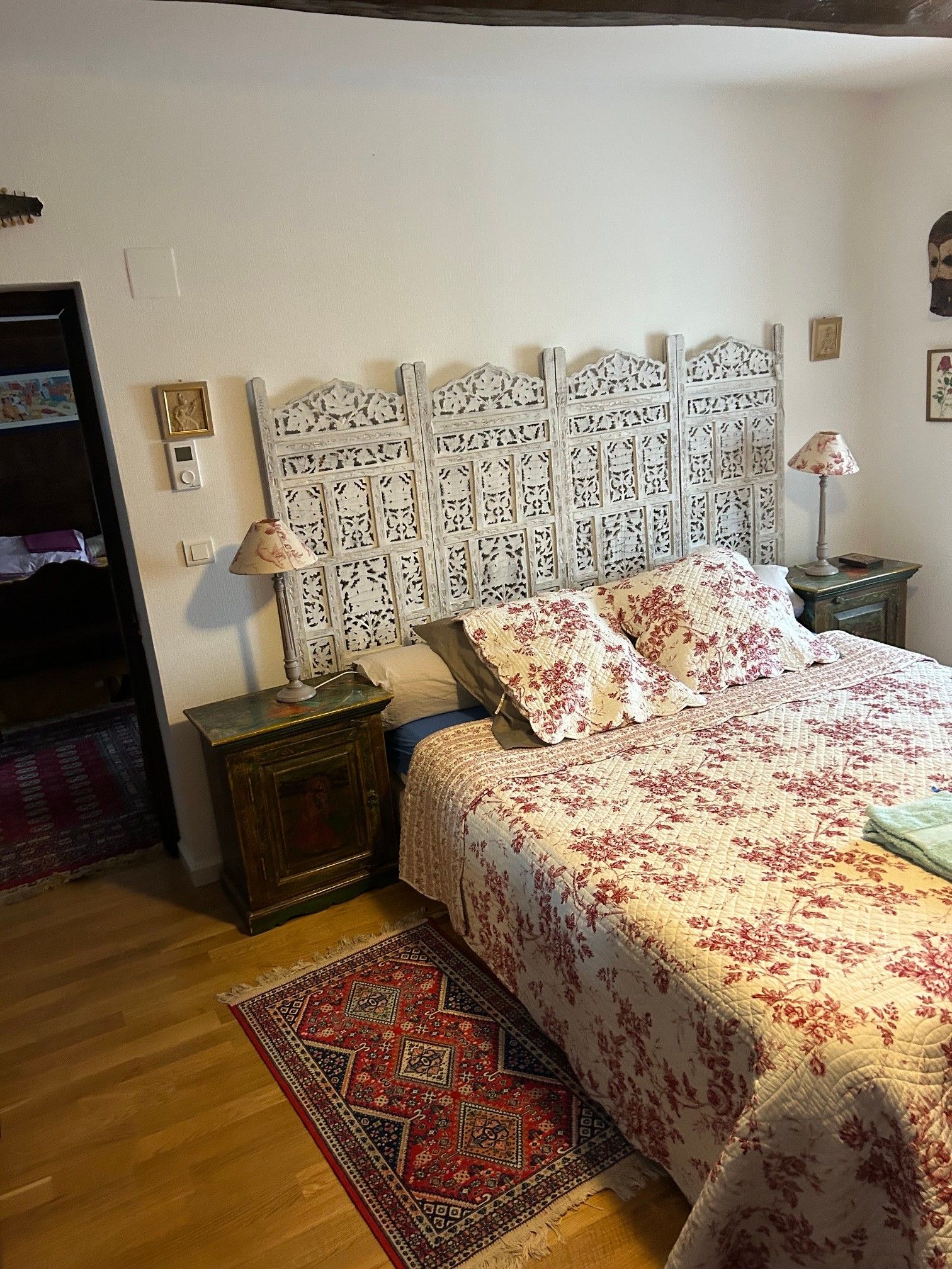 Een slaapkamer met een bed, een nachtkastje, een lamp, een lichtschakelaar aan de muur en een vloerkleed.
