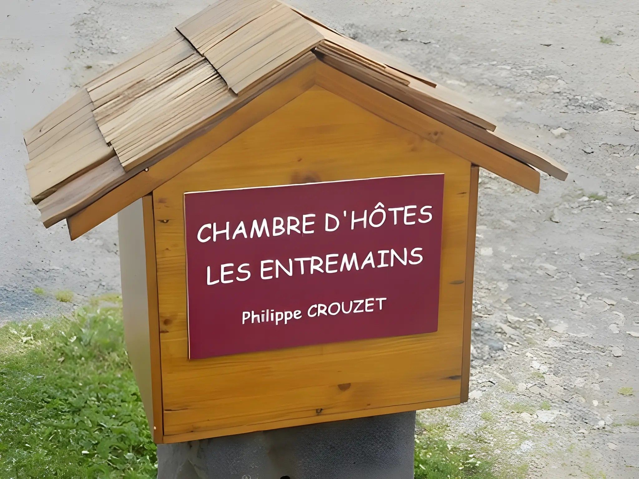 Een houten gebouw met een bord waarop staat 'CHAMBRE D'HÔTES LES ENTREMAJINS PHILIPPE CROUZET'.