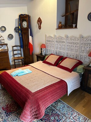 Een slaapkamer met een bed, een houten dressoir, een stoel, een klok en een raam.