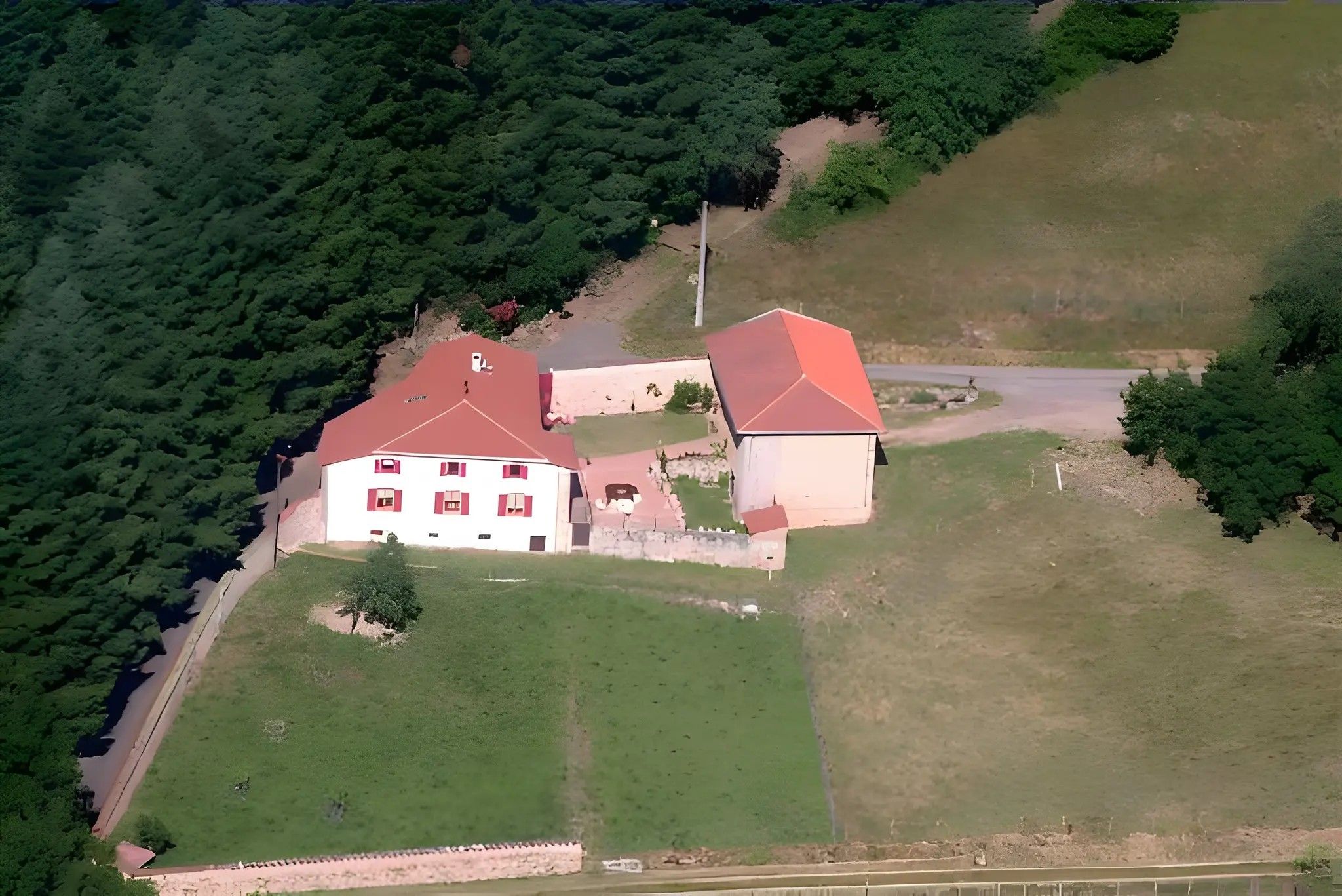 Un edificio de dos pisos con techo rojo, rodeado de campos verdes y árboles frondosos.