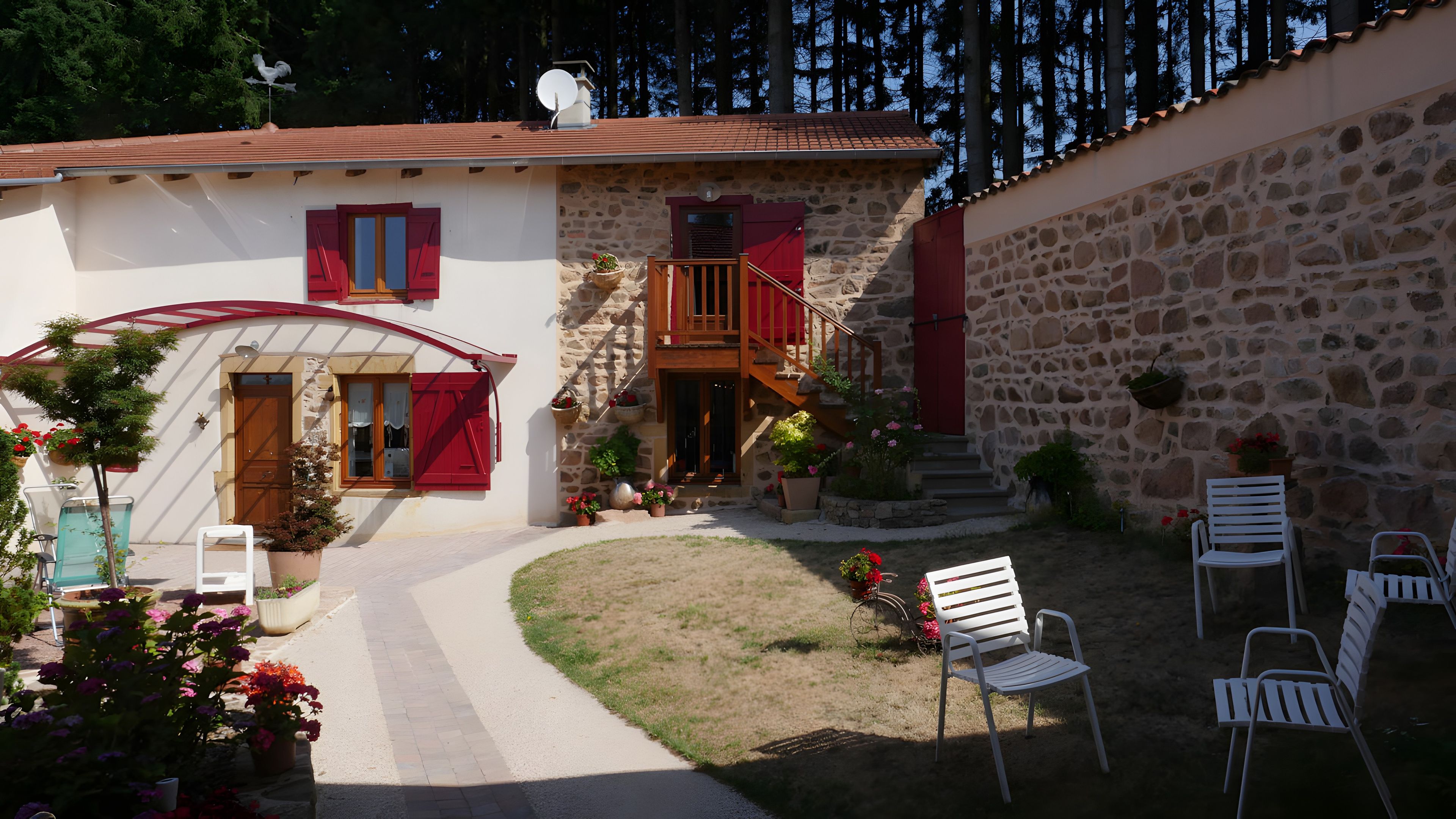 Une maison en pierre avec une porte rouge, un escalier en bois et un espace extérieur aménagé pour s’asseoir.