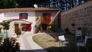 A stone house with a red door, a wooden staircase, and outdoor seating.