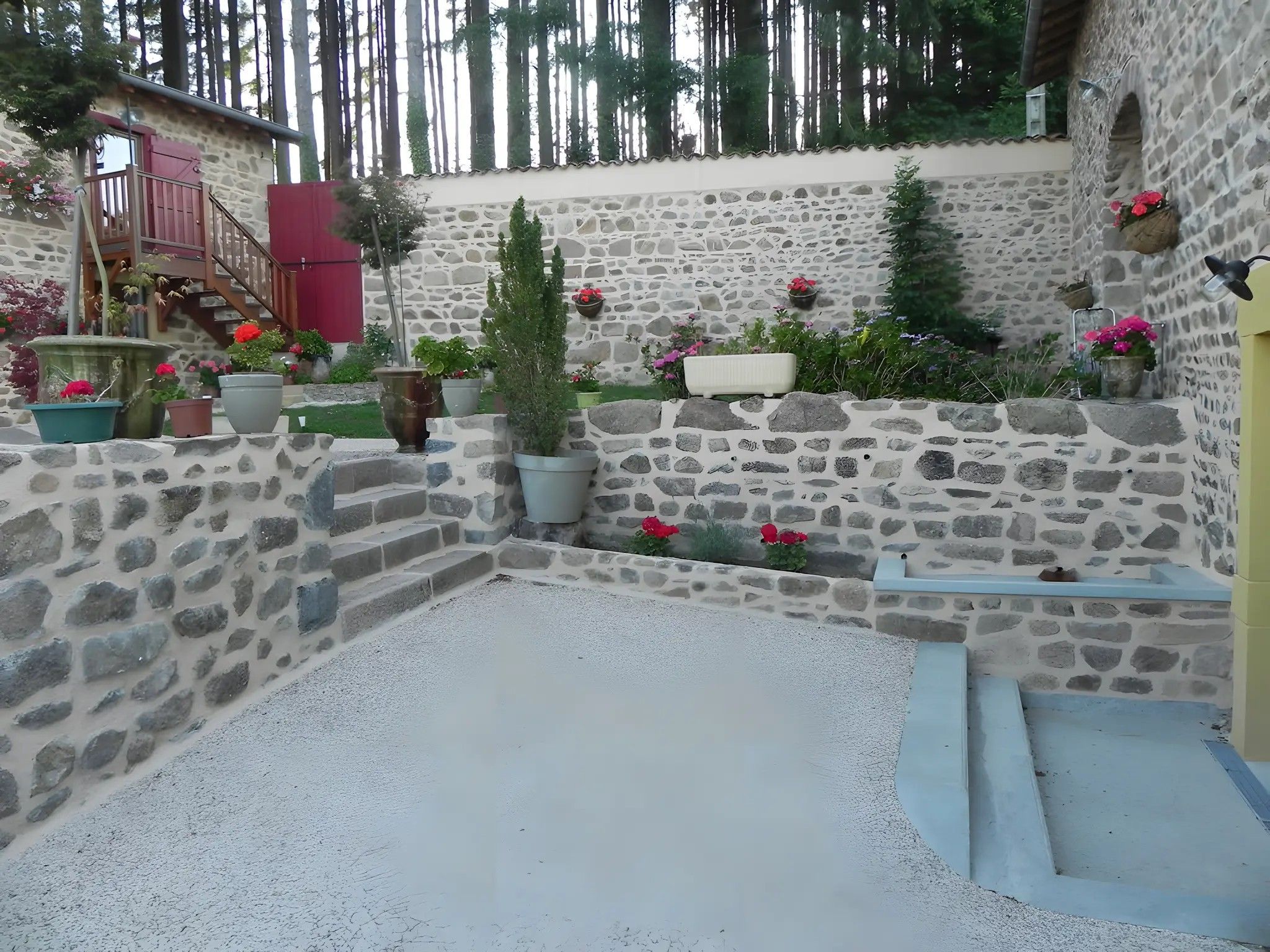 Un patio con paredes de piedra, suelo de grava, plantas en macetas y un pequeño espacio de descanso.