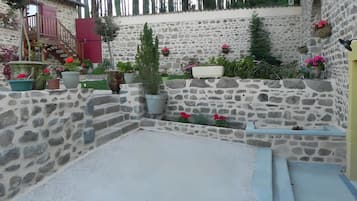 Un patio con paredes de piedra, suelo de grava, plantas en macetas y un pequeño espacio de descanso.