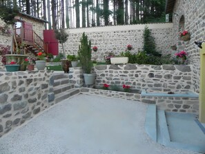 Un patio con paredes de piedra, suelo de grava, plantas en macetas y un pequeño espacio de descanso.