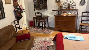 Una habitación tradicional con techo de madera, sofá de cuero marrón, cama con colcha acolchada roja, escritorio de madera y alfombra estampada.