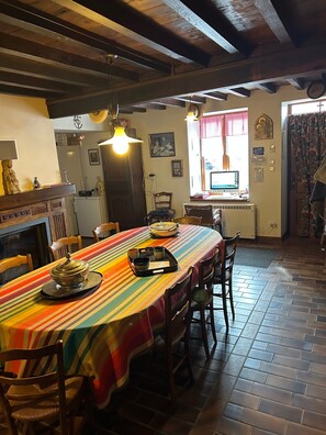 Een eetruimte met een lange tafel, stoelen, een open haard en een raam met gordijnen.