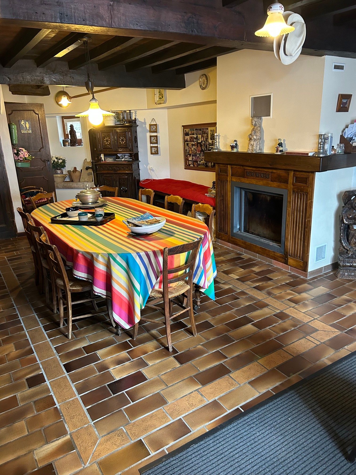 Un comedor con mantel a rayas, sillas de madera, chimenea y suelo de baldosas.