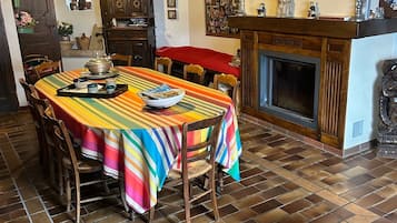 Un comedor con mantel a rayas, sillas de madera, chimenea y suelo de baldosas.