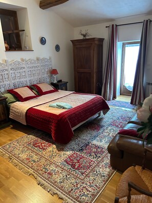 Un dormitorio con una cama grande, un cabecero de madera, una mesita de noche, una lámpara roja, un armario de madera y una alfombra estampada.