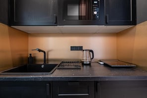 Een keuken met een zwart aanrecht, een koffiezetapparaat, een waterkoker en een magnetron.