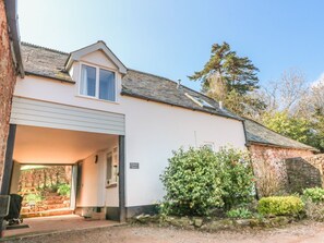 A single-story building with a garage door open, a small window, and a sign labeled 'Upper Barn.' - Upper Barn Cottage (Minehead)