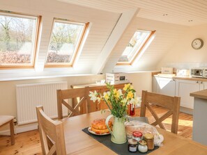 A cozy kitchen with wooden cabinets, a dining table with chairs, and a view of the outdoors through skylights. - Upper Barn Cottage (Minehead)