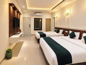 A hotel room with two beds, a TV, an air conditioning unit, and a small potted plant.