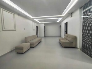 A modern, minimalist room with two sofas and a small ottoman, a patterned wall, and recessed ceiling lighting. - Palette Khadgaon Road Lavha (Nagpur)