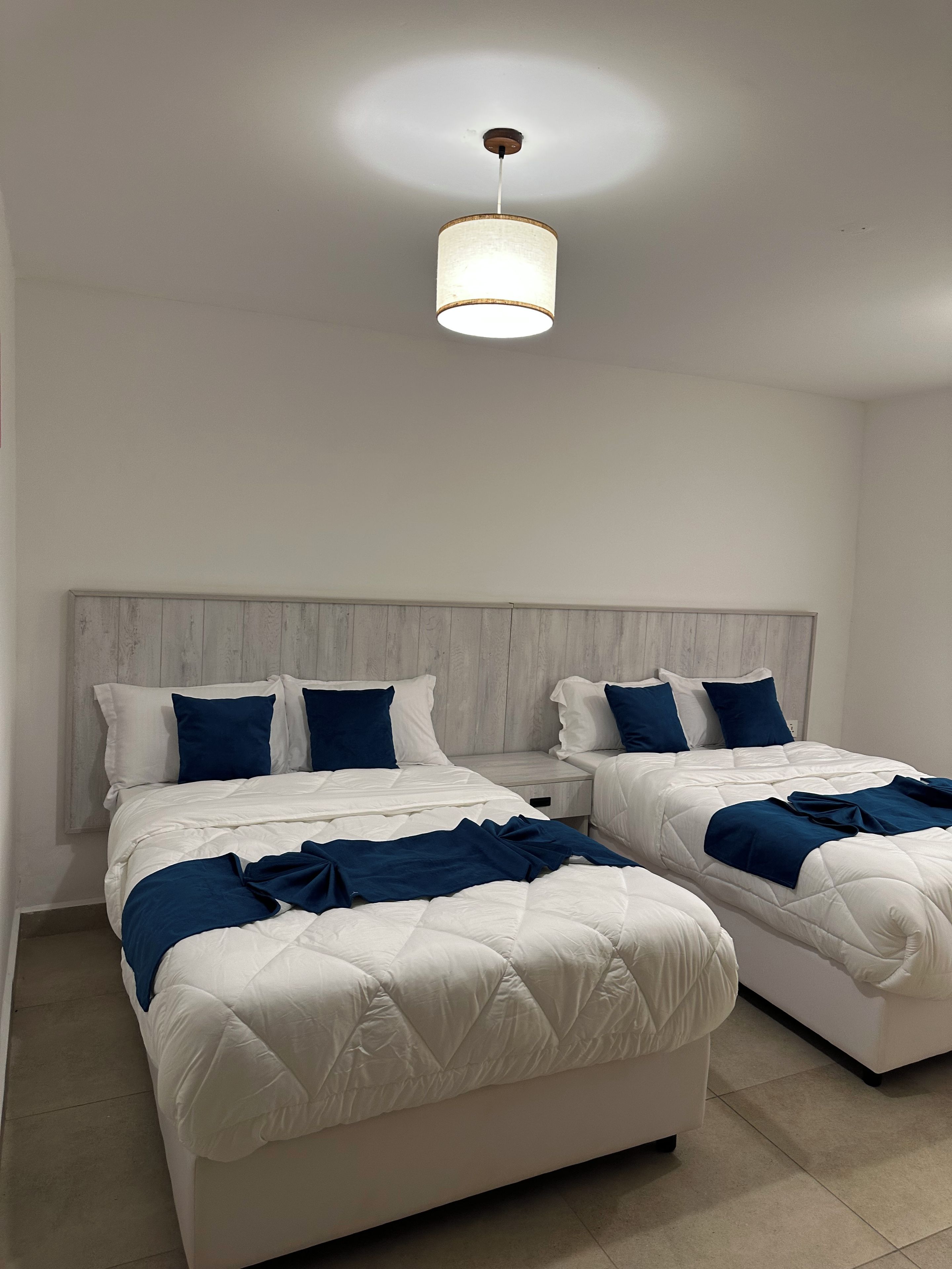 A hotel room with two beds, a wooden headboard, and a hanging light fixture.